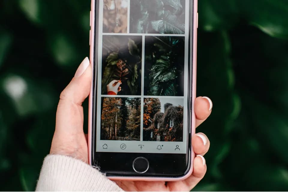 A hand holding a phone that shows a grid of photographs from a social feed